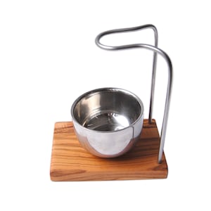 Puede incluir: Un soporte para brocha de afeitar de plata con una base de madera y un soporte de metal. El soporte para brocha está hecho de acero inoxidable y tiene un acabado brillante. La base de madera está hecha de madera de olivo y tiene un patrón de veta natural.