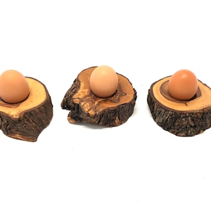 Könnte beinhalten: Drei Eierbecher aus Holz, hergestellt aus Baumrinde, mit einem braunen Ei in jedem Halter.
