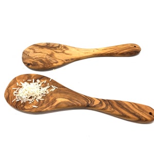 May include: Two olive wood spoons, one with a pile of white rice in the bowl. The spoons have a natural wood grain pattern.
