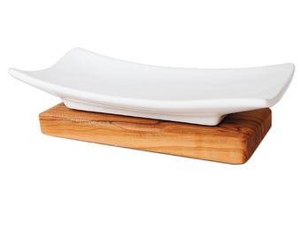 May include: A white rectangular ceramic dish with gently curved sides, resting on a rectangular wooden base. The dish has a smooth, glossy finish. The wooden base has a natural wood grain pattern.