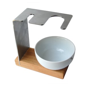 Peut inclure: Un support de rasage en métal argenté avec un bol en céramique blanche et une base en bois. Le support comporte deux crochets pour tenir les rasoirs.