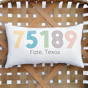May include: A white pillow with a colorful striped design featuring the numbers 75189 and the text "Fate, Texas".