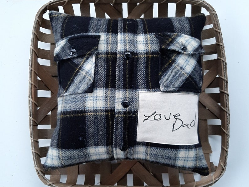 May include: A black and white plaid pillow with a white fabric patch that says "Love Dad". The pillow is in a wooden basket.