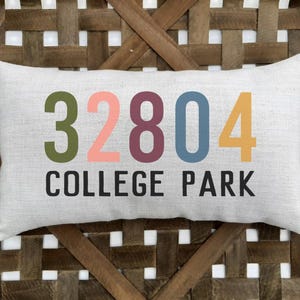 May include: A white cushion with the text "32804 COLLEGE PARK" in colourful letters. The numbers are in different colours: green, pink, maroon, blue, and yellow.