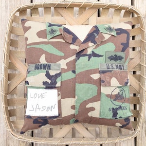 May include: A camouflage pillow with a U.S. Navy patch, a "Seabees" patch, and a name tag that reads "BROWN". The pillow also has a handwritten note that says "Love Jason".