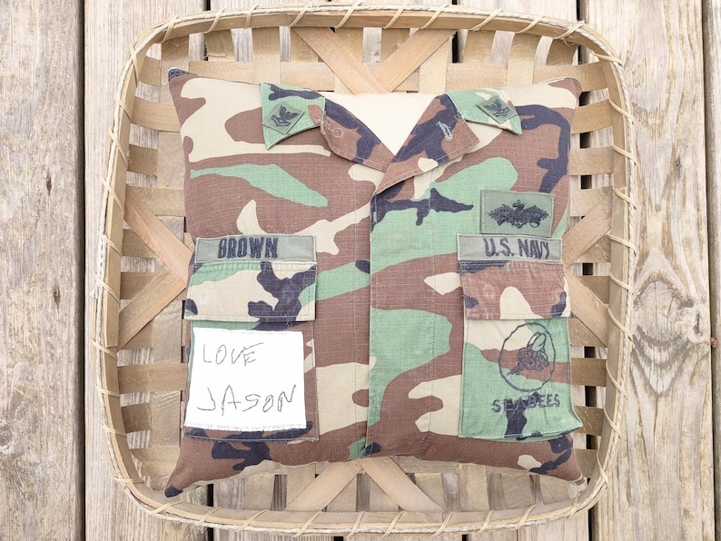 May include: A camouflage pillow with a U.S. Navy patch, a "Seabees" patch, and a name tag that reads "BROWN". The pillow also has a handwritten note that says "Love Jason".