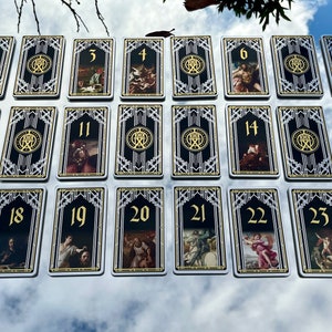 Puede incluir: Un juego de 23 cartas de tarot con diseños art déco en negro y dorado. Cada carta presenta una ilustración única y un número del 1 al 23.