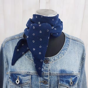 Könnte beinhalten: Ein marineblauer Schal mit weißem Herzmuster liegt über einer Jeansjacke. Der Schal ist dreieckig gebunden, mit herabhängenden Enden. Die Jacke hat ein klassisches Design mit Knopfverschlüssen und Taschen.