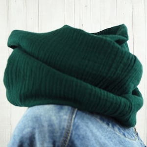 Könnte beinhalten: Ein dunkelgrüner Infinity-Schal aus weichem, strukturiertem Stoff. Der Schal ist gefaltet und über eine Jeansjacke gelegt.