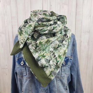 Könnte beinhalten: Ein grüner und weißer Schal mit tropischem Blättermuster. Der Schal ist um eine Jeansjacke gewickelt. Der Schal hat einen grünen Rand und ein sternförmiges Etikett.