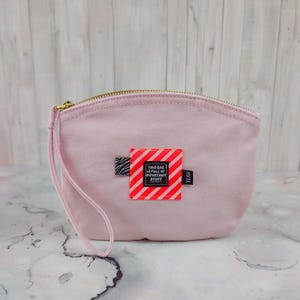 Op de afbeelding: Een lichtroze canvas etui met een zwart-wit gestreept patch waarop in rode letters staat "This bag is full of important stuff". Het etui heeft een zwart-wit zebraprint patch en een zwart label met de tekst "YEH!"