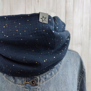 Könnte beinhalten: Ein marineblauer Schalkragen-Schal mit goldenen Glitzerpunkten. Der Schal hat ein kleines schwarzes Leder-Etikett mit einem Stern.