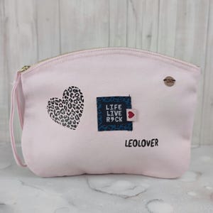 Op de afbeelding: Roze canvas make-up tas met een zwart-wit luipaardprint hart, een blauwe patch met de tekst "LIFE LIVE ROCK", een rood hart en de tekst "LEOLOVER".