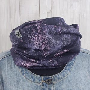 Könnte beinhalten: Ein dunkelblau-lila gemusterter Halstuch mit einem Stern-Logo-Etikett. Der Stoff hat ein gesprenkeltes Design mit rosa Akzenten. Der Halswärmer wird auf einer Jeansjacke präsentiert.