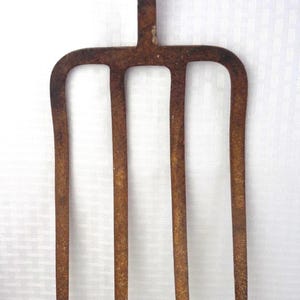 May include: A rusty, antique garden fork with four tines and a handle. The metal tool has a weathered appearance, suggesting age and use. The fork is designed for turning soil and other gardening tasks.