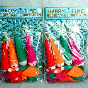 May include: Two identical packages of Happy Time Holiday Decorations, each containing four cone-shaped figures with fringed hats in red, orange, green, and pink. The figures have round faces and colorful skirts, packaged in clear plastic with green patterned backing.