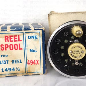 May include: Vintage Pflueger Medalist reel with original box. The reel is black and silver with a cream-colored handle and center cap. The box is blue and cream with the text "REEL SPOOL FOR MEDALIST REEL".
