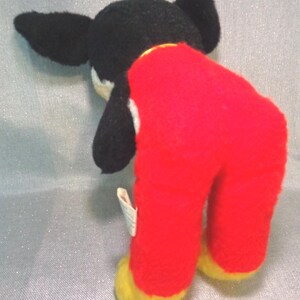 Puede incluir: Juguete de peluche negro y blanco con pantalones rojos y pies amarillos. El juguete est&aacute; de pie con la cabeza inclinada hacia abajo.