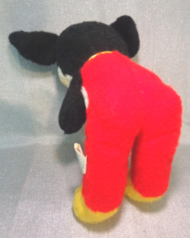 Puede incluir: Juguete de peluche negro y blanco con pantalones rojos y pies amarillos. El juguete est&aacute; de pie con la cabeza inclinada hacia abajo.