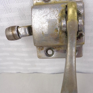 May include: A vintage metal latch with a silver finish and a brass handle. The latch has a rectangular base with two screw holes and a lever for opening and closing. The handle is a curved shape.
