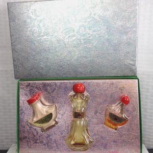 May include: A vintage perfume set in a silver box with a green trim. The set includes three glass perfume bottles with red stoppers. The bottles are in a pink, embossed tray.
