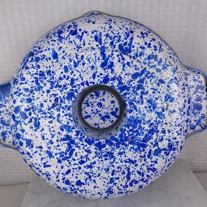 May include: A round, white and blue speckled bundt pan with a central tube and two handles. The pan has a blue rim and a dark gray tube. The speckled pattern is a mix of blue and white.