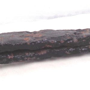 May include: A large, antique iron nail with a rounded head and a long, tapering shank. The nail is heavily rusted, displaying a dark brown color. The head has a distinctive curved shape, and the overall design suggests a historical or vintage item.