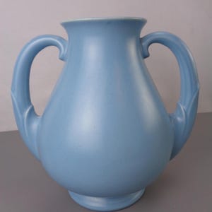 May include: A light blue ceramic vase with two handles. The vase has a rounded body and a flared lip.