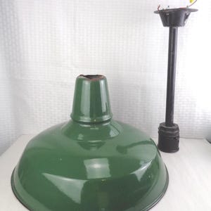 May include: A green metal pendant light shade with a matching green top section. A black metal pole and fixture are positioned to the right. The light fixture is a vintage industrial style.