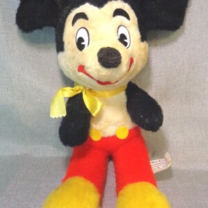 Puede incluir: Juguete de peluche vintage Mickey Mouse con pelaje negro, lazo amarillo, pantalones rojos y zapatos amarillos. El juguete tiene una etiqueta de Walt Disney Productions.