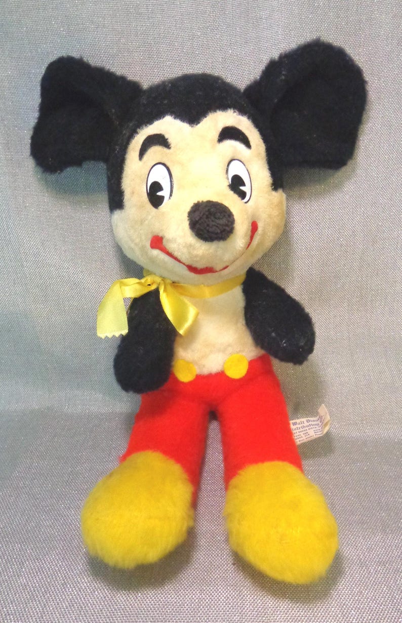 Puede incluir: Juguete de peluche vintage Mickey Mouse con pelaje negro, lazo amarillo, pantalones rojos y zapatos amarillos. El juguete tiene una etiqueta de Walt Disney Productions.