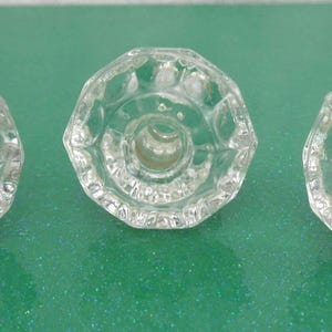 May include: Three clear, faceted glass cabinet knobs. Each knob has a circular design with a central hole for mounting. The knobs are arranged in a row against a green background.