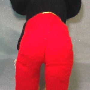 Puede incluir: Juguete de peluche negro y rojo con orejas grandes. El juguete lleva pantalones rojos con ribetes amarillos.