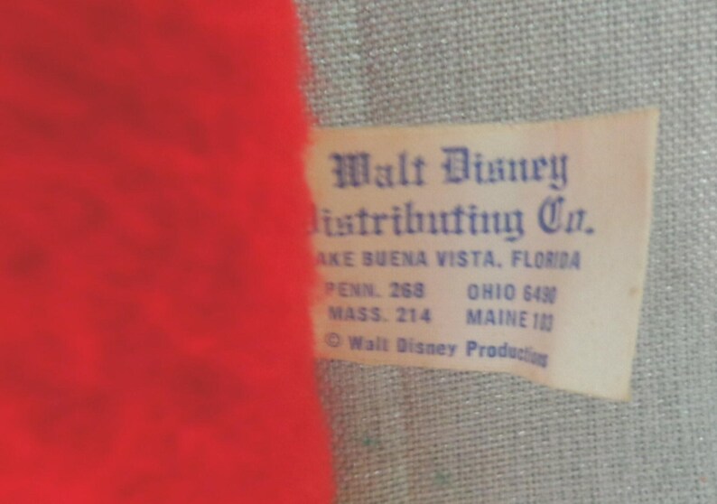 Puede incluir: Una etiqueta blanca con texto azul que dice "Walt Disney Distributing Co.". La etiqueta tambi&eacute;n incluye la direcci&oacute;n de la empresa: "Lake Buena Vista, Florida", y la informaci&oacute;n de contacto para Pensilvania, Ohio, Massachusetts y Maine.