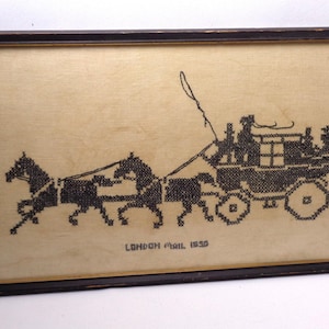 May include: A framed cross-stitch embroidery on beige fabric featuring a black thread design of a horse-drawn carriage with two horses and a driver. The text "LONDON MAIL 1830" is stitched in black below the carriage, all enclosed in a dark wood frame.