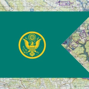 May include: A teal flag with a gold emblem featuring an eagle and a circular design. The flag has a unique shape with a cut-out section on the right side. The background is a map.