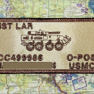 May include: Tan rectangular patch with brown border, featuring the text "1ST LAR" and "USMC". A military vehicle is in the center. Additional text includes "CC499986" and "O-POS". The patch is set against a map background.