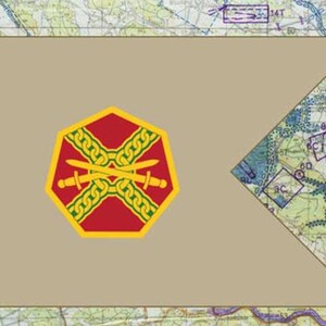 May include: A tan flag with a red and gold emblem featuring crossed swords and a chain design. The flag has a map background with various markings and symbols, including the text "29TOW".