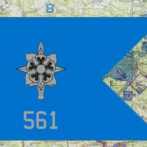 May include: A blue flag with a white and gray emblem and the number 561 in white. The flag has a map background with various markings and symbols.