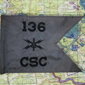 May include: A gray flag with the number "136" and the letters "CSC" printed in black. A black emblem featuring a sword and lightning bolts is centered on the flag. The flag is set against a map background.