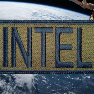 May include: Embroidered patch with the word "INTEL" in navy blue letters on a tan background. The patch has a navy blue border and is set against a backdrop of Earth and a space station.