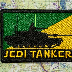 May include: Embroidered patch featuring a black tank silhouette with a green and yellow background. The text "JEDI TANKER" is in yellow. The patch is rectangular and has a black border.