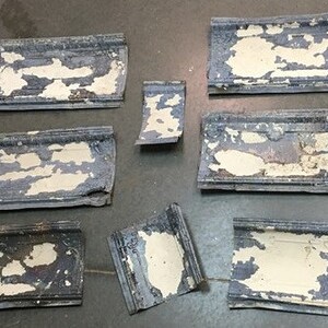 May include: A collection of eight vintage, blue and white, metal tiles with a distressed, chipped paint finish. The tiles have a decorative, raised border.