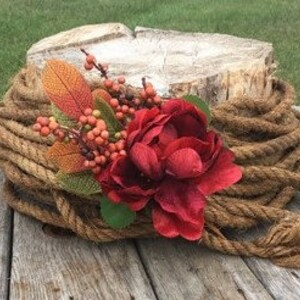 May include: A rustic wooden cake stand with a rope border and a red flower and fall foliage decoration.