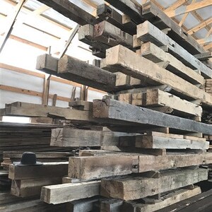 Puede incluir: Una gran pila de vigas de madera recuperadas, algunas con un acabado gris oscuro, en un almac&eacute;n.