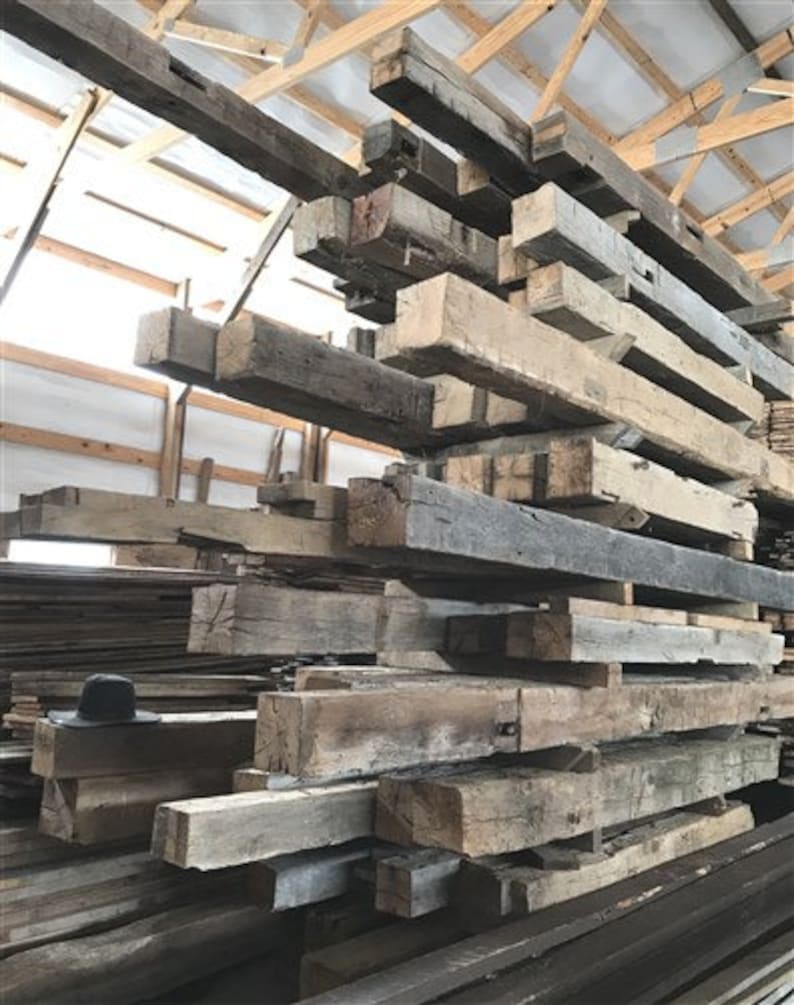 Puede incluir: Una gran pila de vigas de madera recuperadas, algunas con un acabado gris oscuro, en un almac&eacute;n.