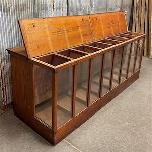 May include: Antique wooden display case with glass fronts and hinged lids. The case has eight compartments and is labeled "Grocer - Grain, Beans, Barley, Hominy, Etc. Hall Hardware Co."