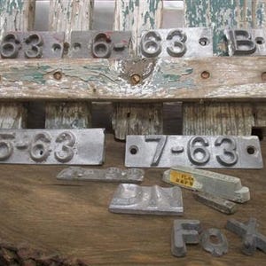 Peut inclure: Un ensemble de tampons à chiffres en métal vintage, comprenant les chiffres 5, 6, 7 et 13, ainsi que les lettres "B" et "Fox". Les tampons sont disposés sur une surface en bois vieilli.