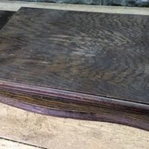 May include: A dark brown wooden desk organiser with a rectangular top and a lower, wider base. The wood grain is visible, and the edges are slightly rounded. The organiser sits on a wooden surface.