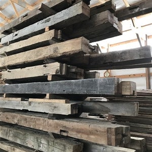 Puede incluir: Una pila de vigas de madera recuperada, algunas con nudos e imperfecciones visibles, listas para usar en una variedad de proyectos.